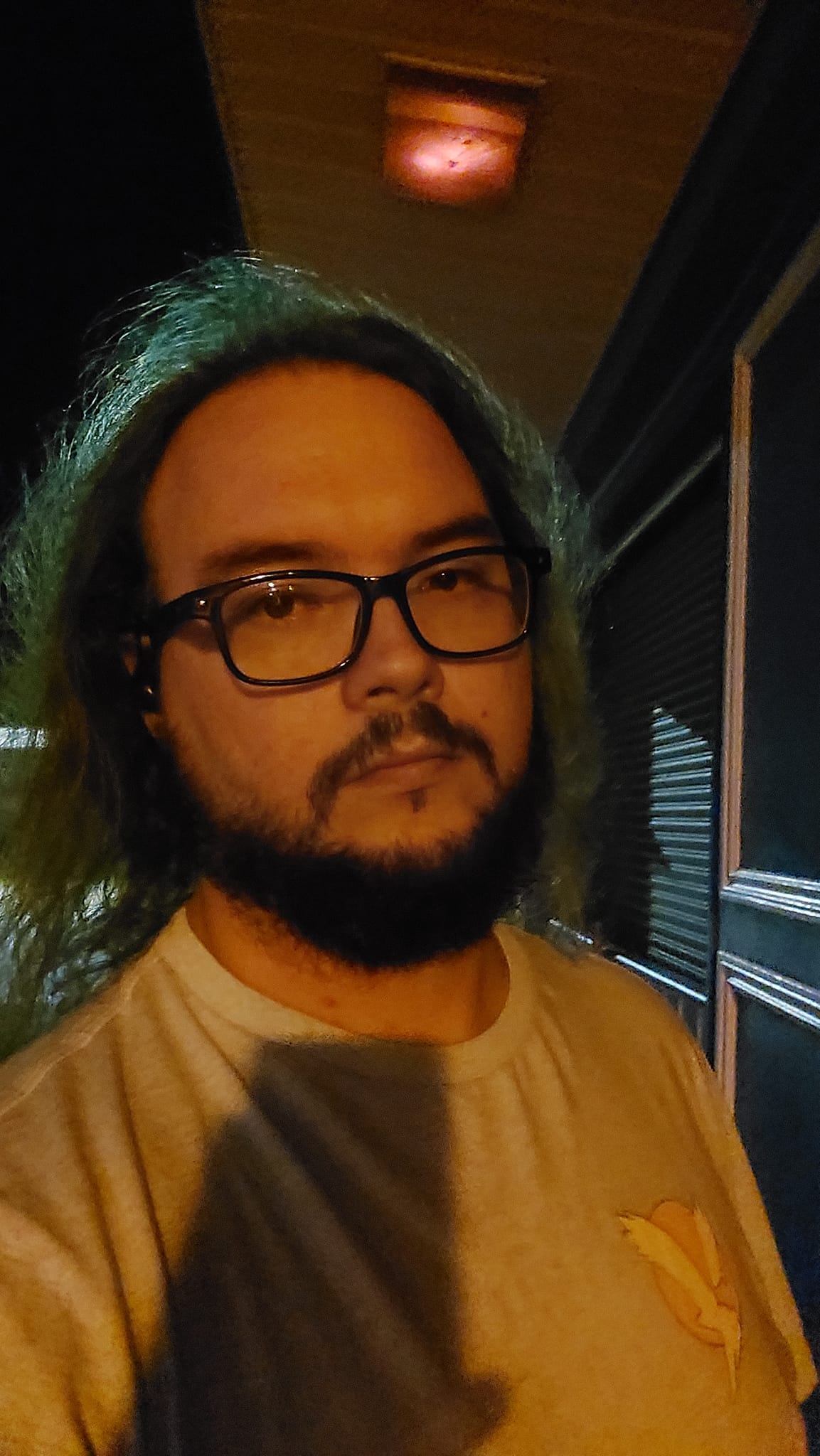 A man with hair that looks brown and shirt that looks yellow stands under a monochromatic street light